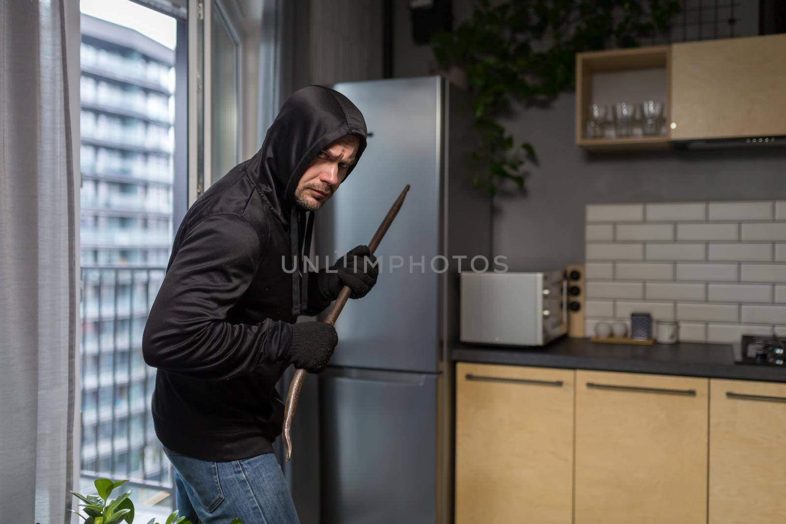 Young male robber in dark clothes carefully and quietly enters through the balcony window by voronaman