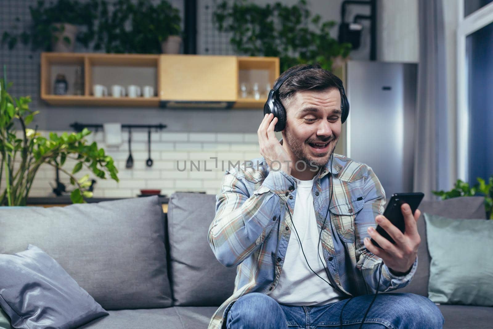 Happy man at home smiling and listening to music from phone uses music by voronaman