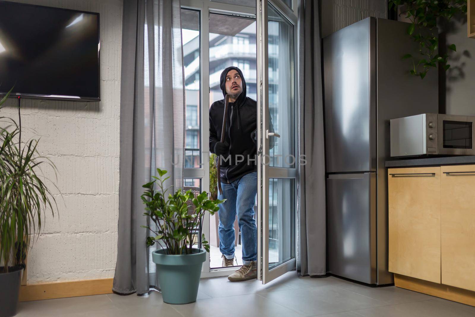 Young male robber in dark clothes carefully and quietly enters through the balcony window by voronaman