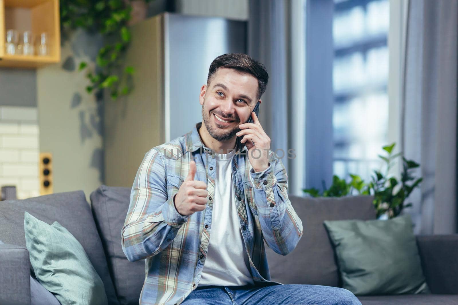 Happy and cheerful man at home sitting on the couch smiling and talking on the phone