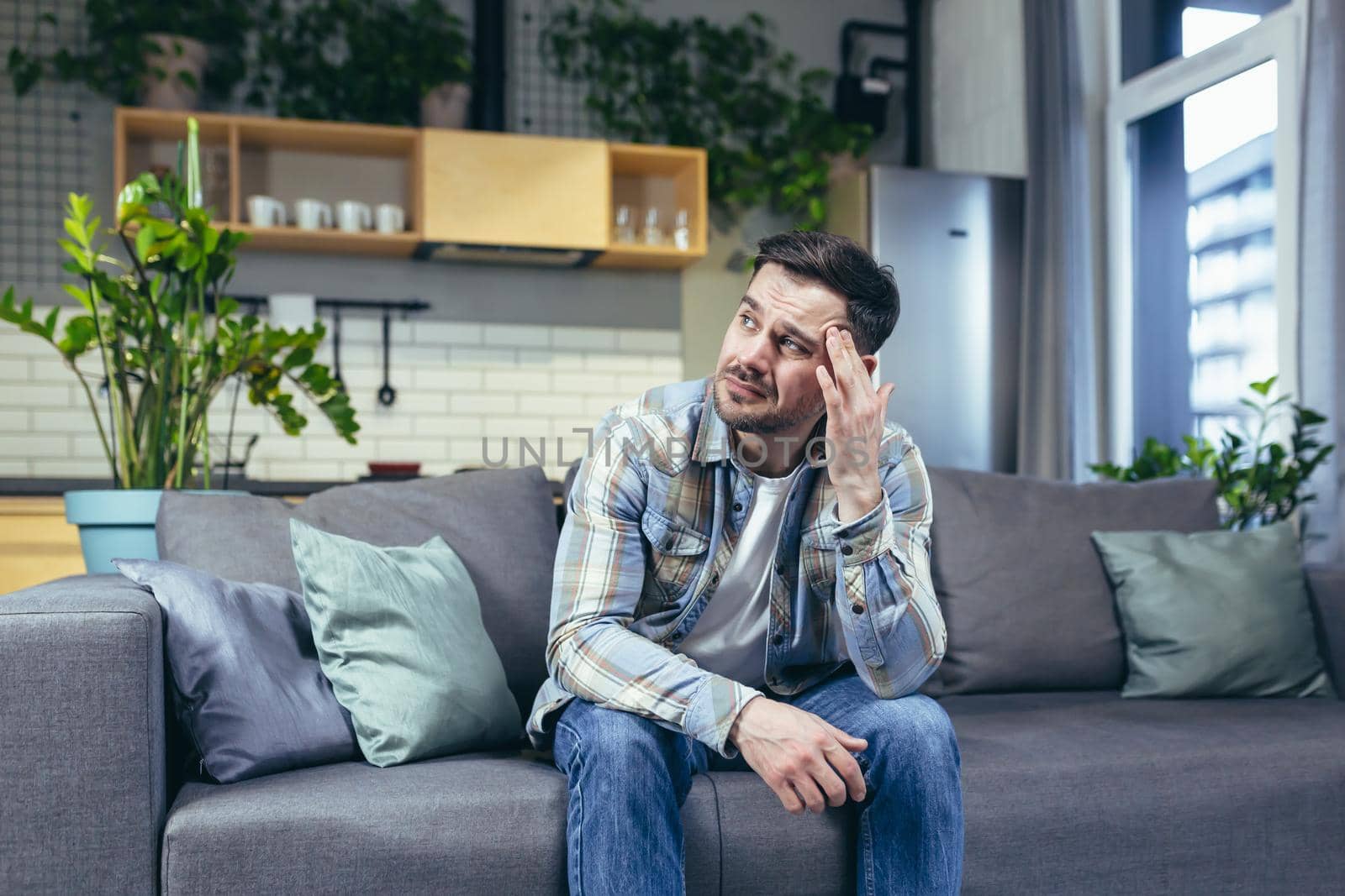 The sick man is sitting alone at home on the couch, has a severe headache