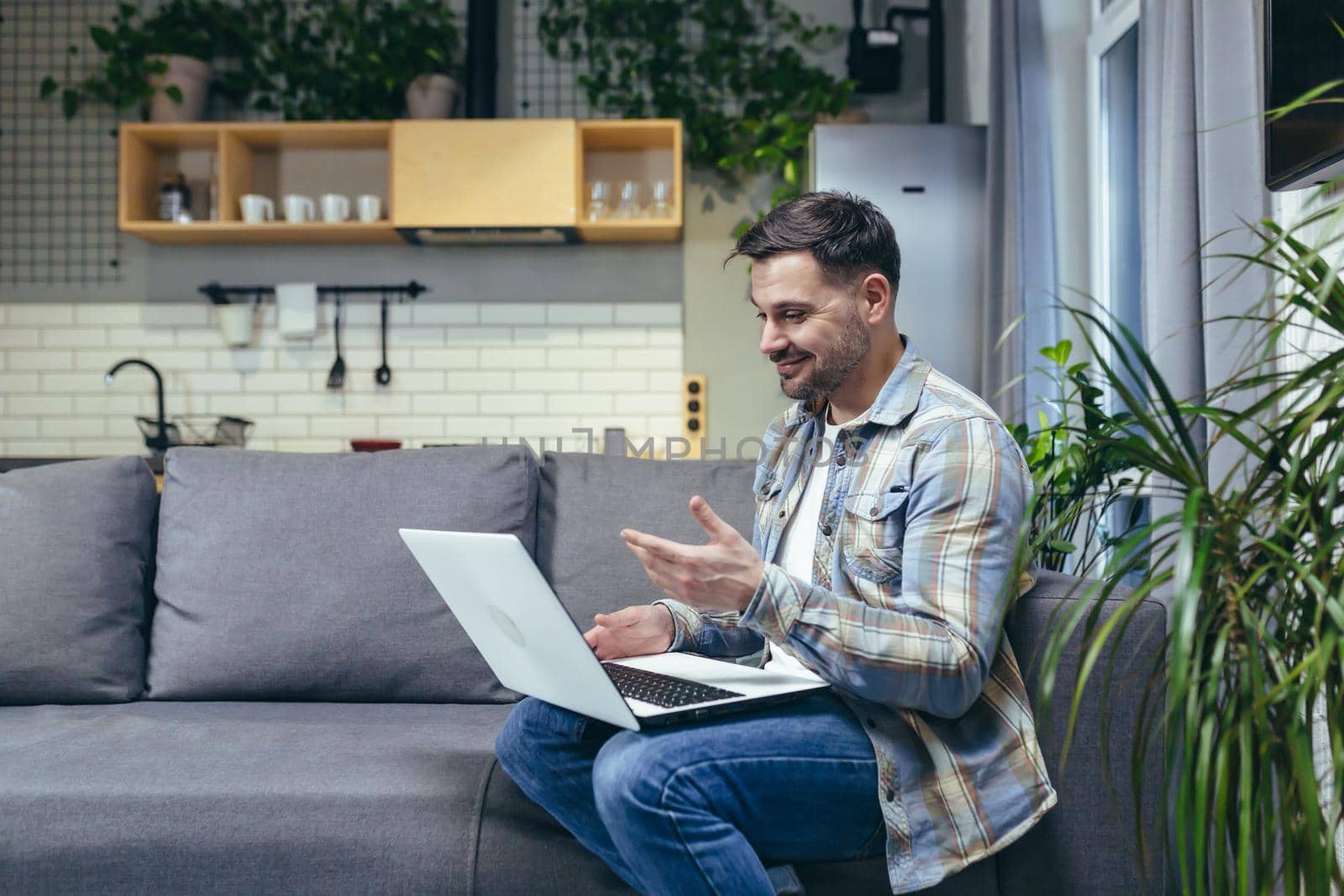 Young man working from home with laptop. Talks on video call. Sitting on the couch.