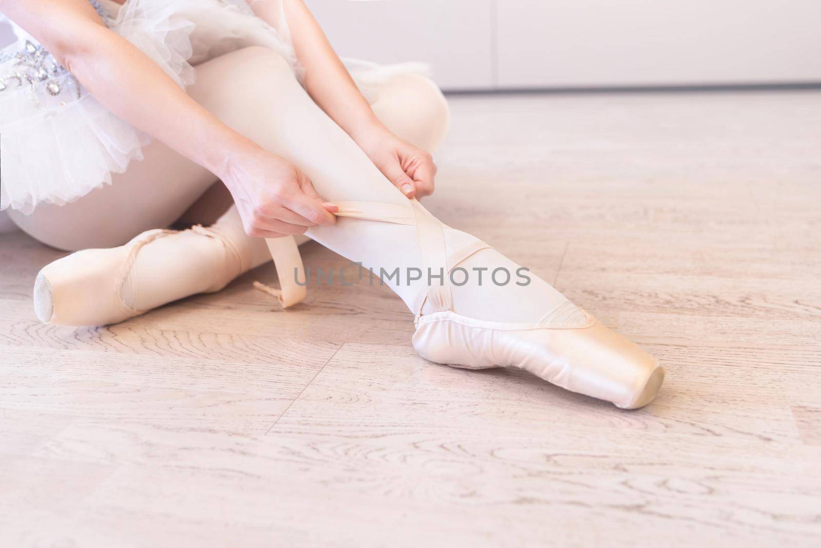 A ballerina sitting on the floor tying her ballet shoes by Nickstock