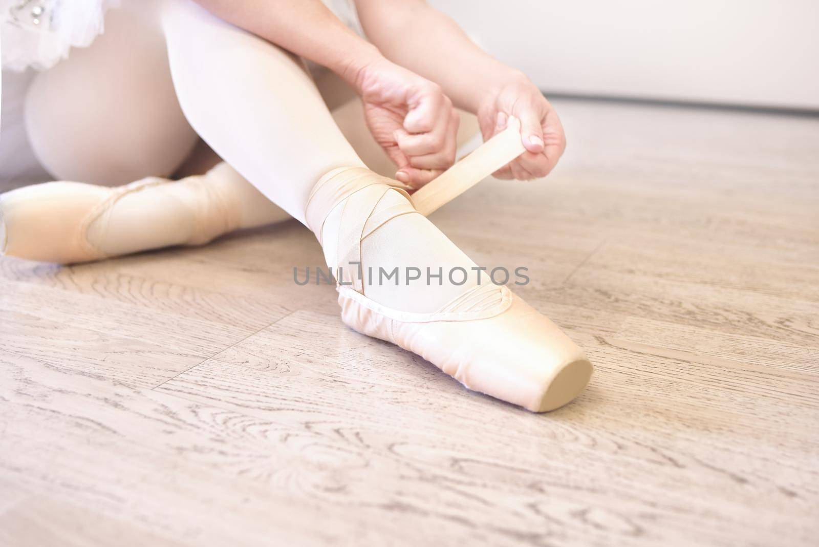 A ballerina sitting on the floor tying her ballet shoes. close view