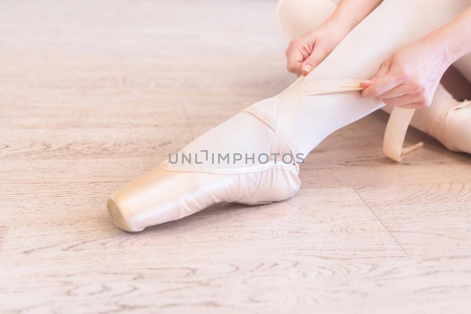 A ballerina sitting on the floor tying her ballet shoes. close view