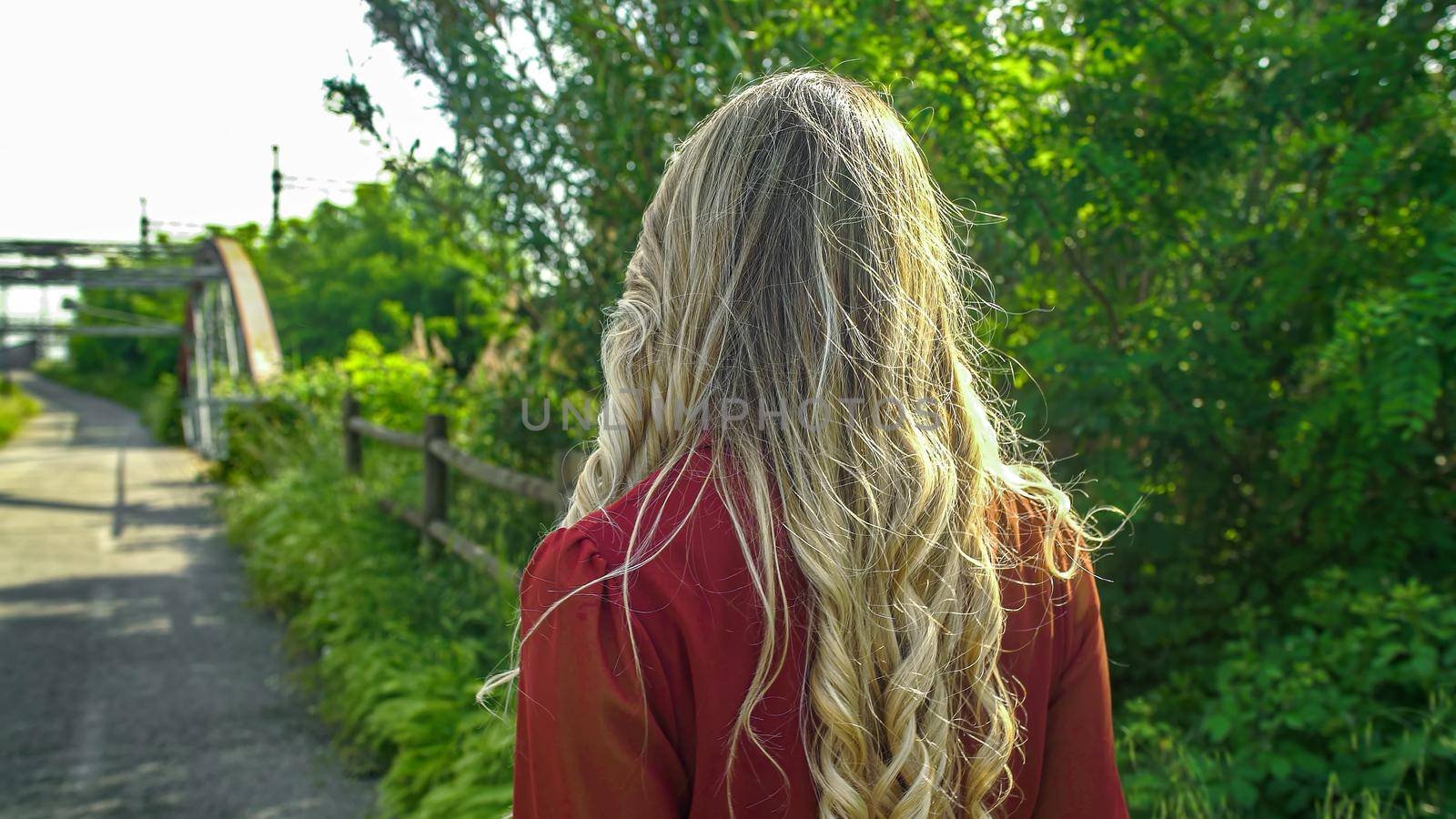 Back view of woman with beautiful long blond hair on the walking track of a park