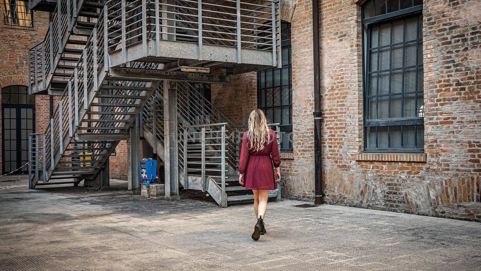 Girl with long curls walks slowly and turns back brick wall and stair background