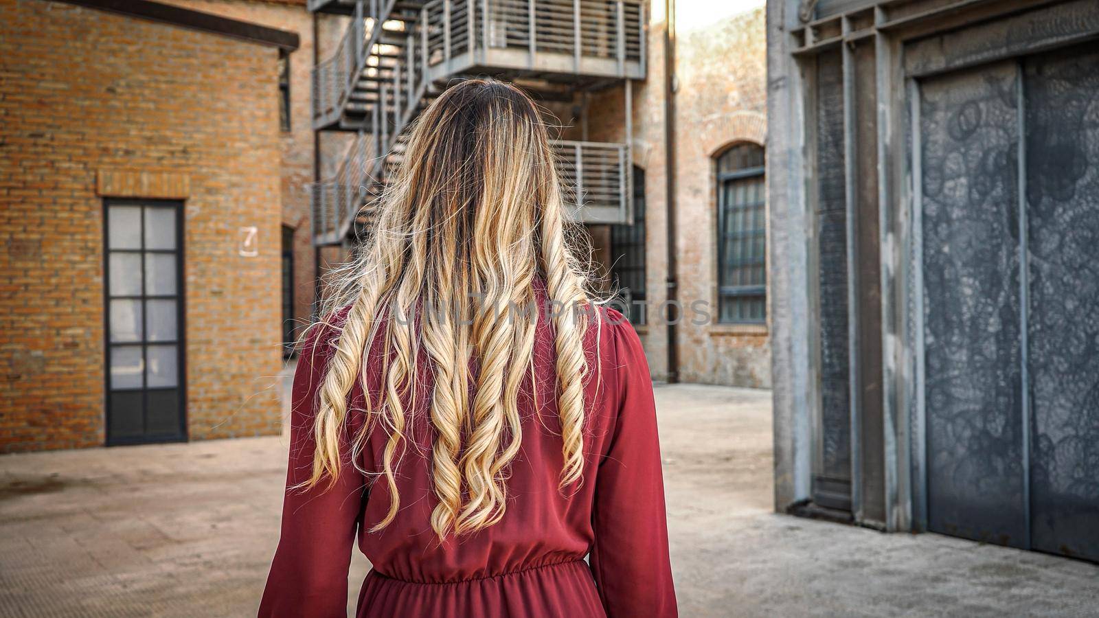 Girl with long curls walks slowly and turns back brick wall and stair background