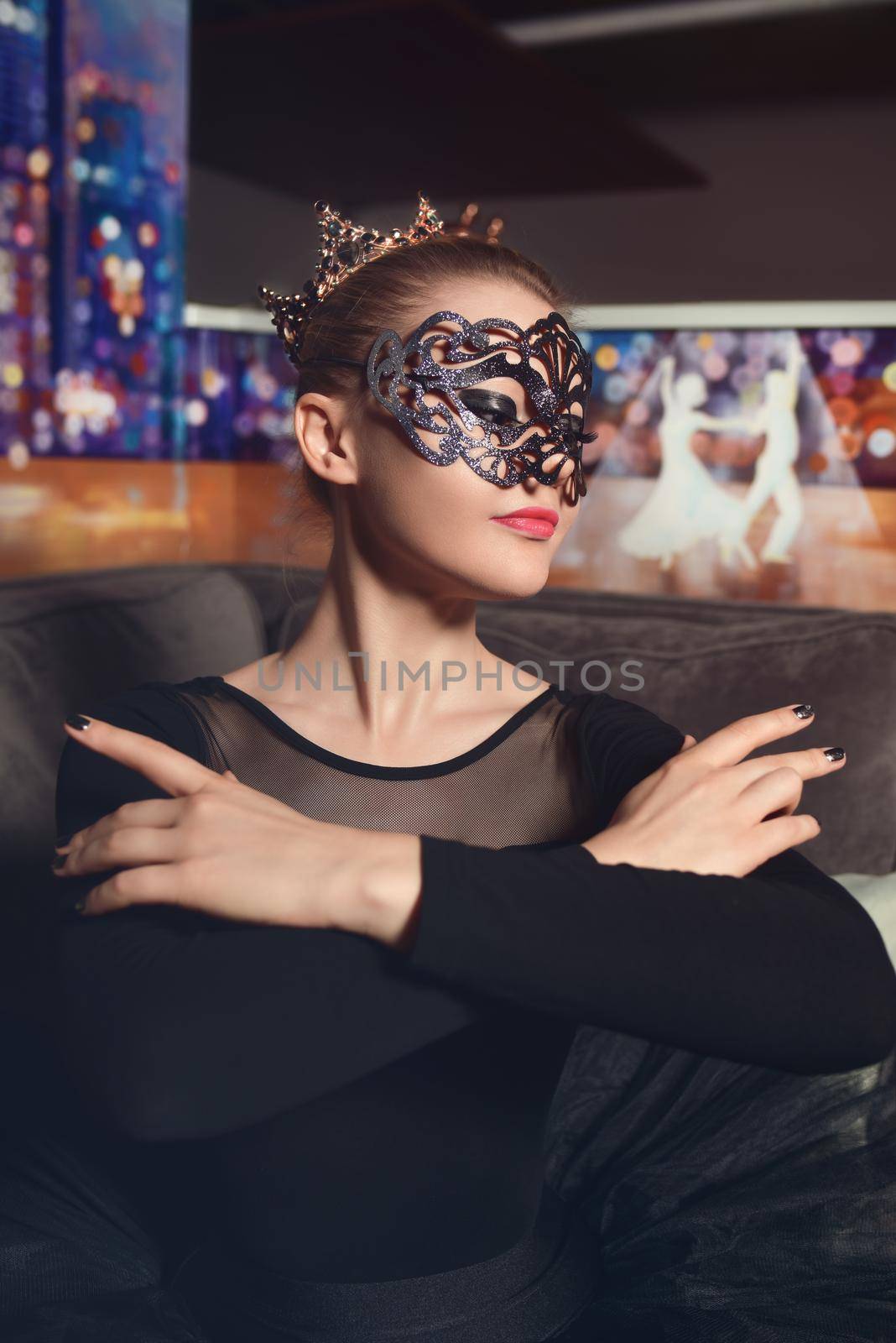 Portrait of a beautiful model ballerina wearing a crown and carnival mask in a black tutu in the studio. black swan ballerina