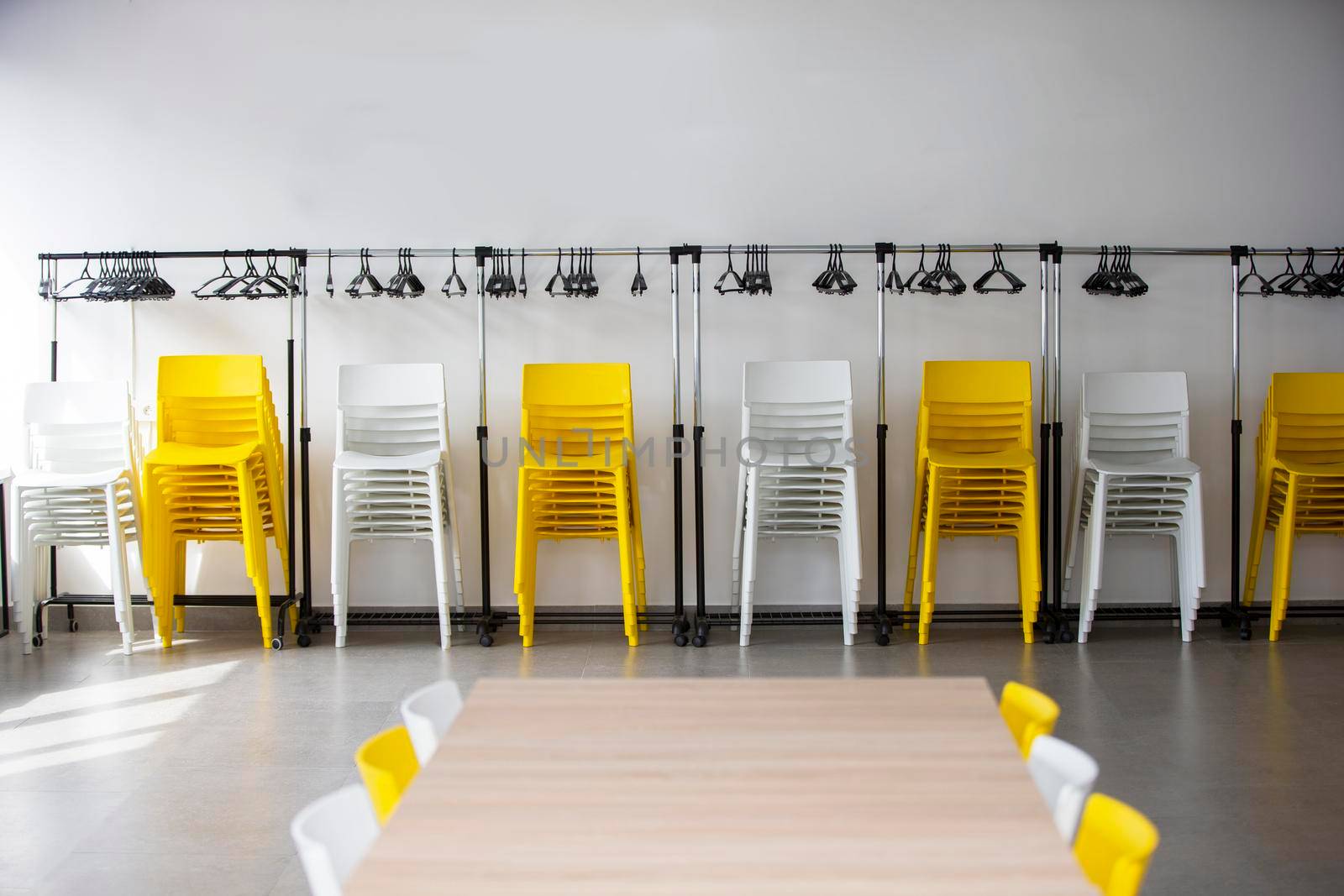 Rows of white and yellow plastic chairs against a white wall in an empty office. Empty meeting room.