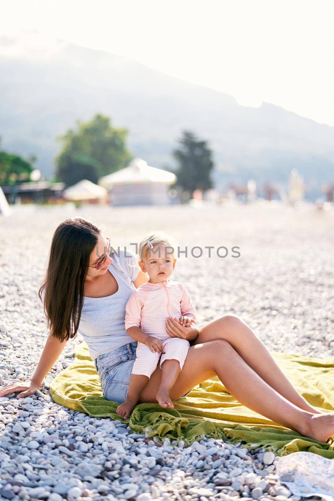 Little girl sits in her mother arms on a pebble beach by Nadtochiy