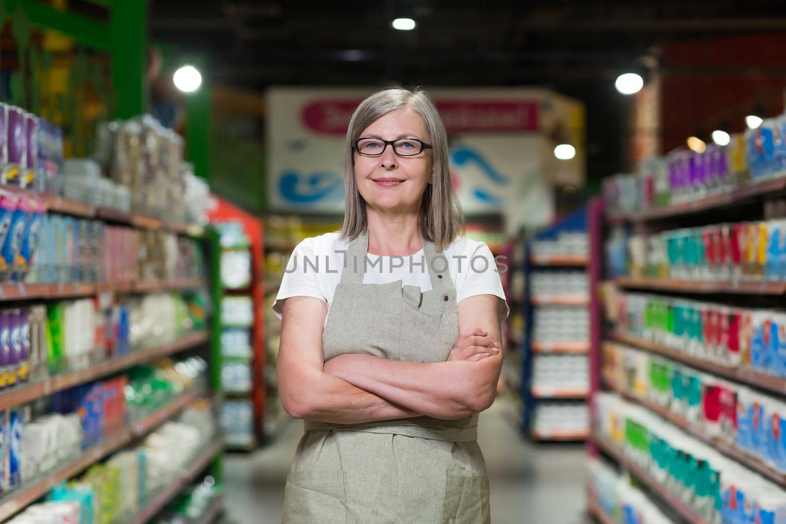 Portrait of happy senior woman grocery store employee with arms crossed smiling and looking at camera