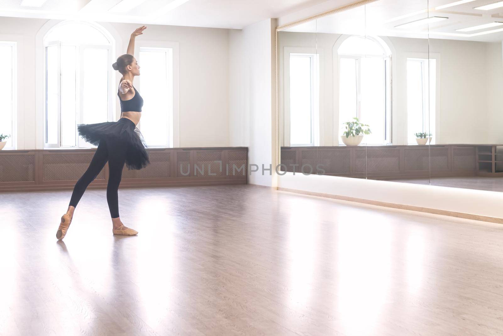 graceful ballerina in a black tutu performs ballet exercises in front of a mirror in the studio