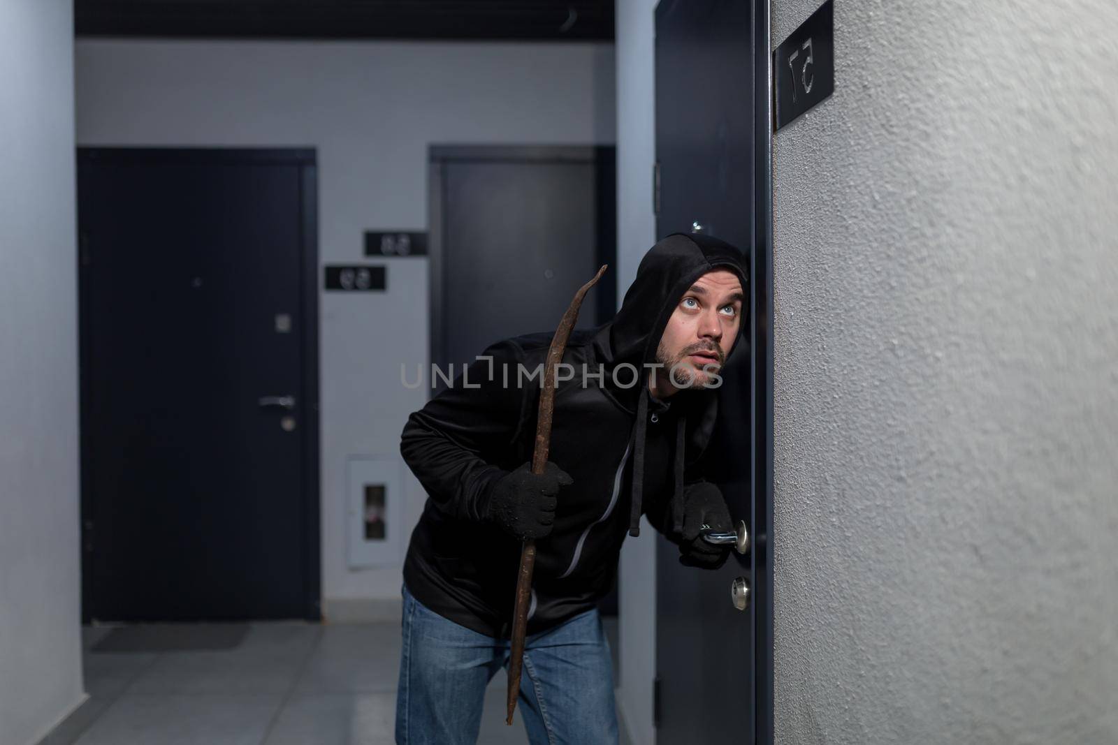 A young male robber in dark clothes stands carefully and quietly at the door of the by voronaman