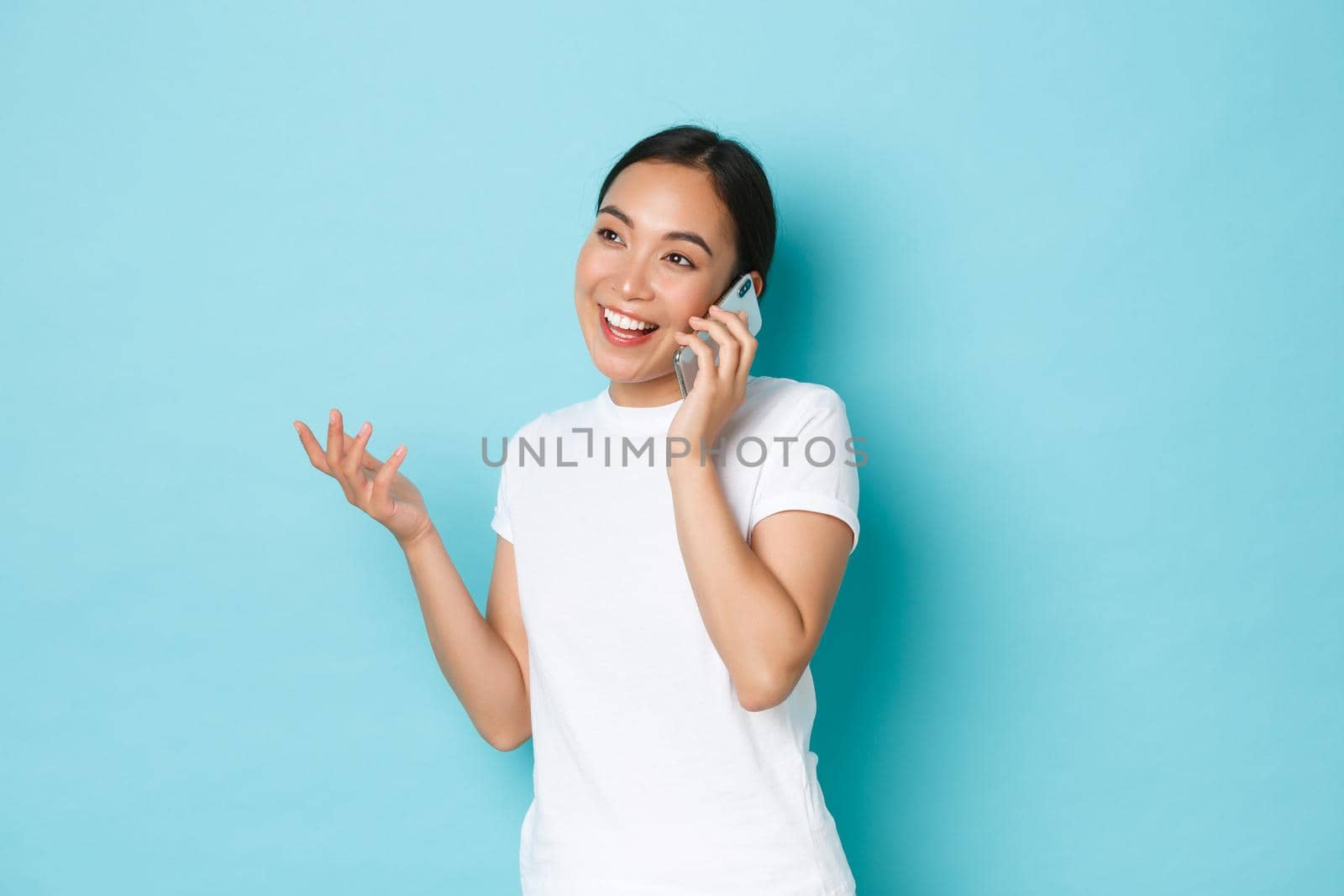 Lifestyle, people and beauty concept. Young attractive asain girl discussing something, having cheerful conversation, talking on mobile phone and gesturing, smiling upbeat.