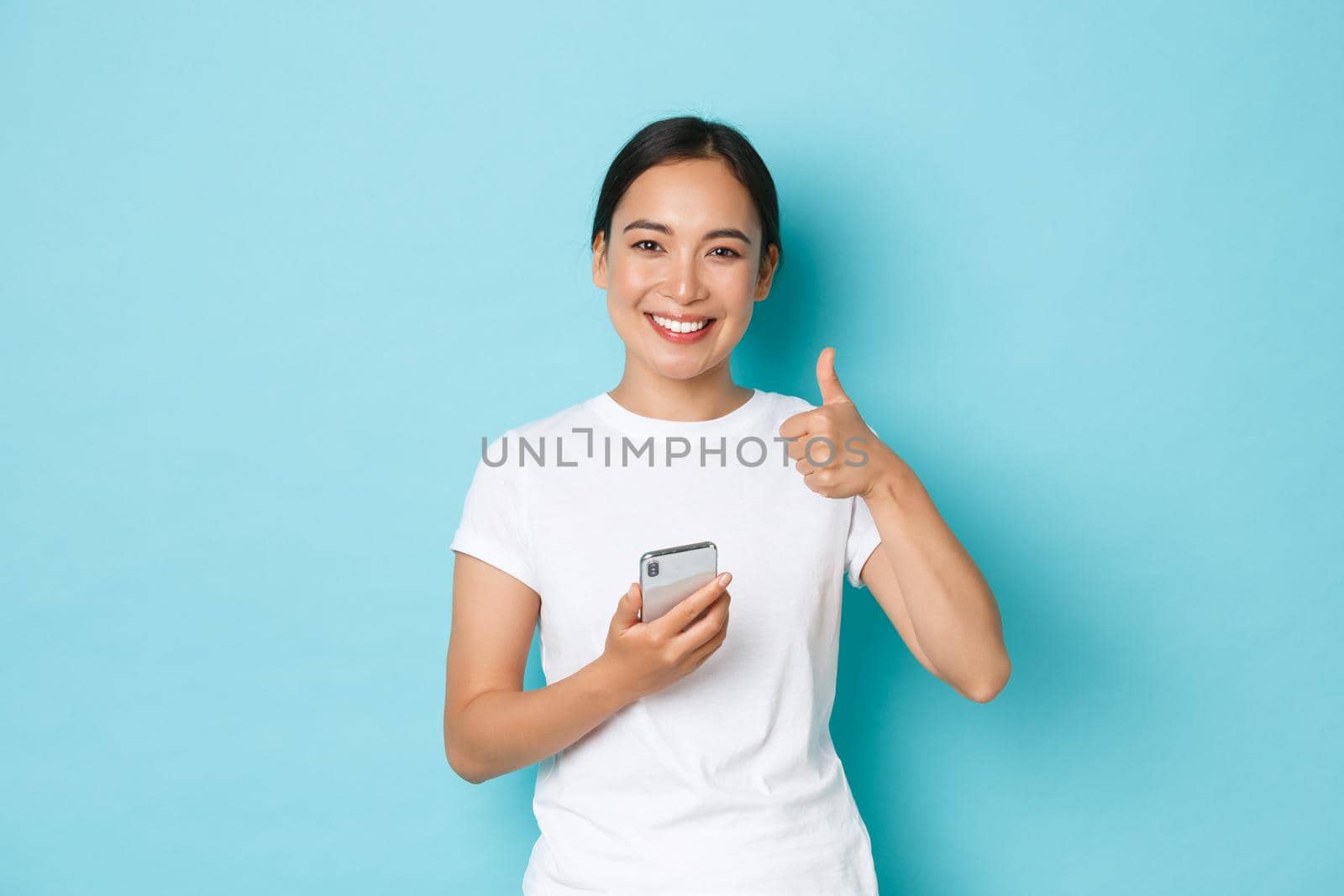 Lifestyle, technology and e-commerce concept. Satisfied beautiful asian female customer, client of online shop, leave positive feedback, holding smartphone and showing thumbs-up gesture.