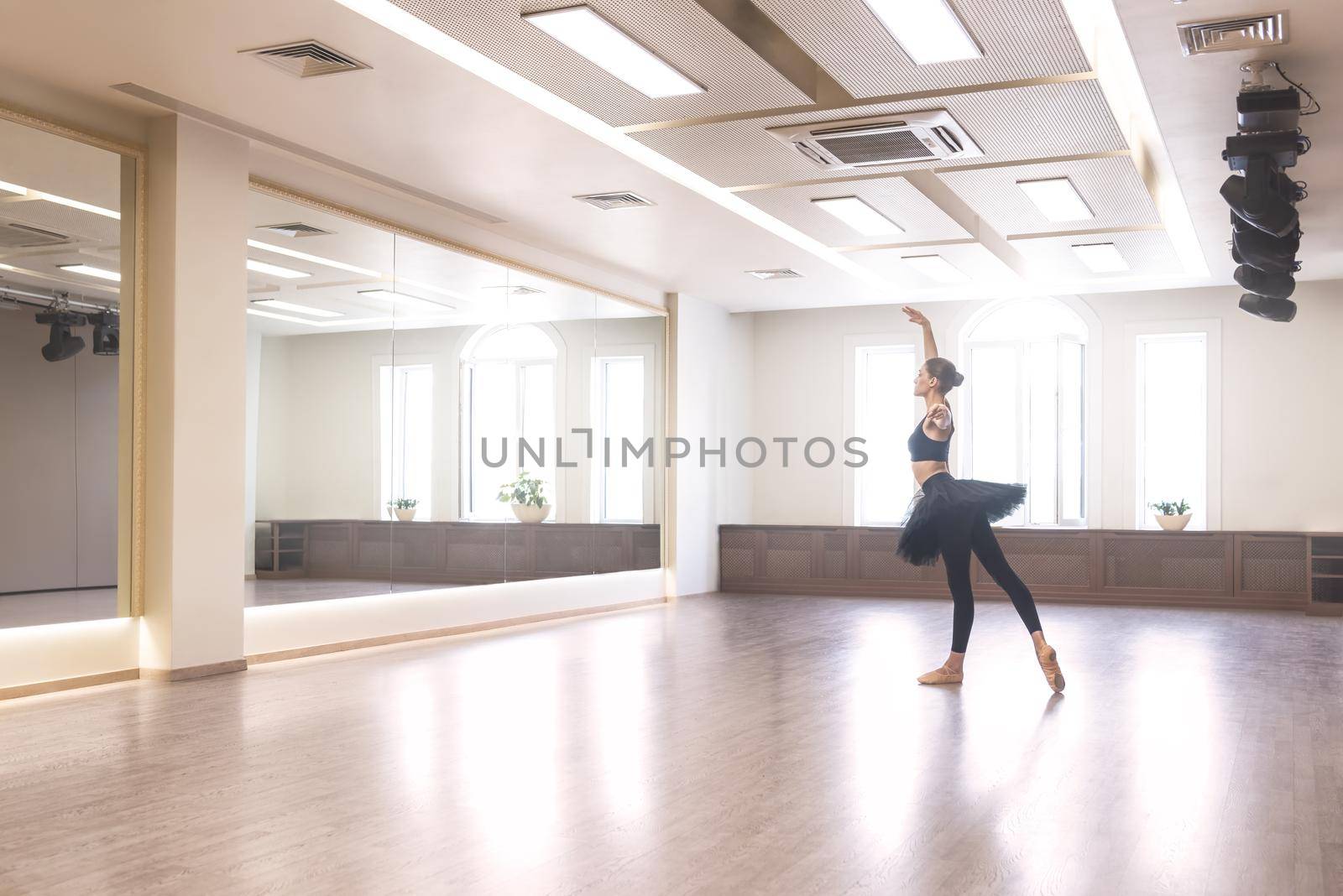 A graceful ballet dancer in a black tutu performs ballet exercises in front of a mirror in the studio