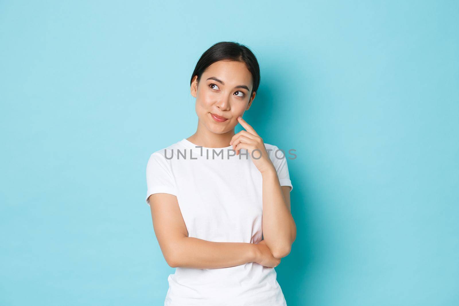 Lifestyle, beauty and shopping concept. Thoughtful asian female student, girl in casual clothes looking upper left corner and thinking, pondering decision, making choice over white background by Benzoix