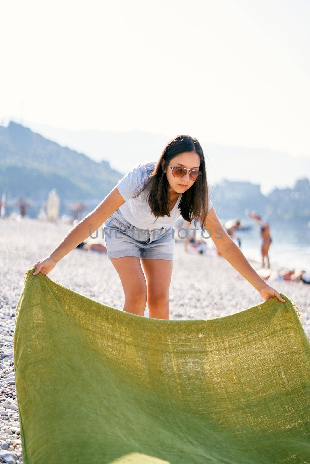 Young woman spreads a blanket on a pebble beach. High quality photo