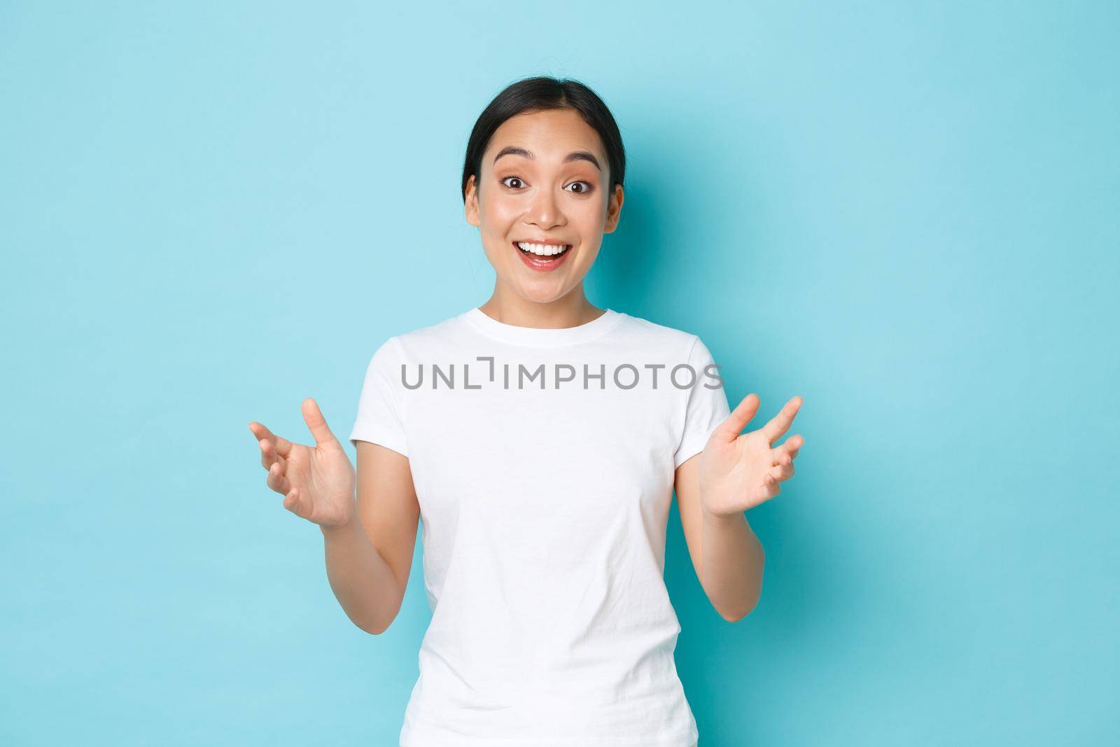 Lifestyle, beauty and shopping concept. Surprised rejoicing asian female react to amazing news, clasp hands and smiling fascinated, looking euphoric, praise person did good job, blue background.