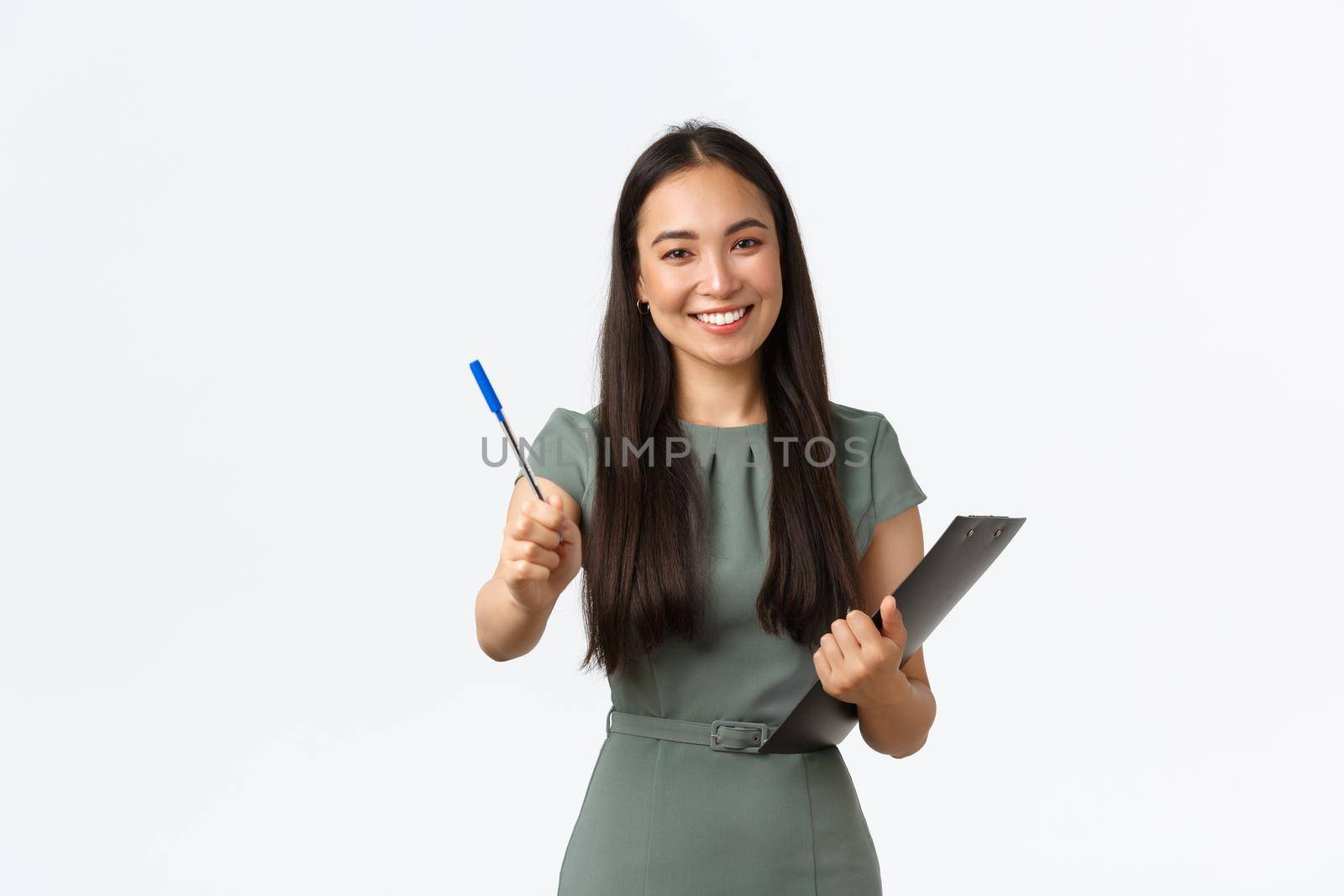 Smiling beautiful asian female shop assistant, employee asking to sign blank or shipping form, giving you pen as holding clipboard with documents, standing white background.