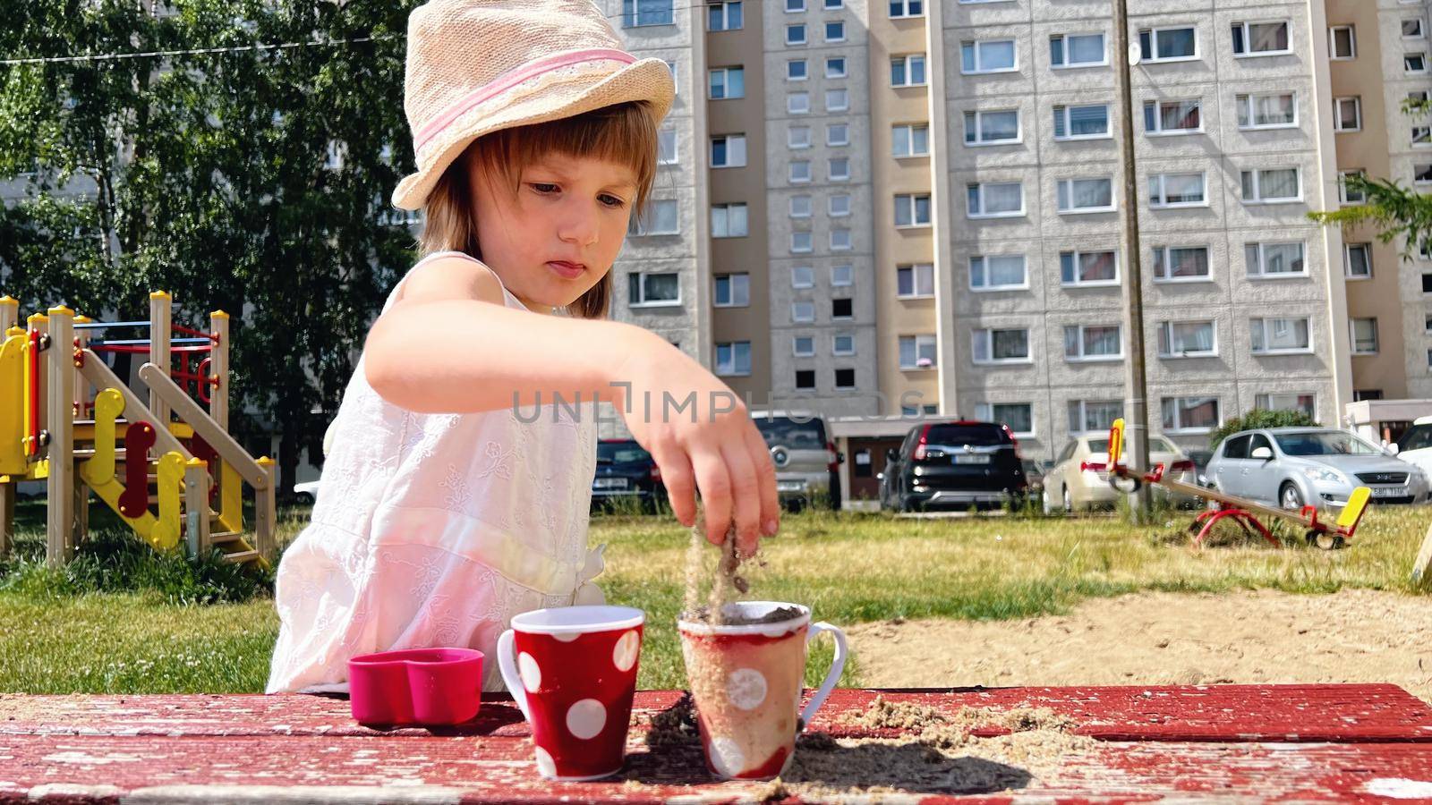 SMALL GIRL IN SUMMER DRESS playing with sand in the backyard of urban block houses in Tallinn, Estonia