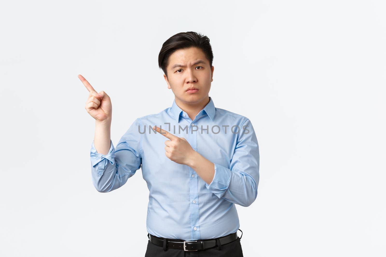 Business, finance and people concept. Disappointed frowning asian businessman in blue shirt pointing upper left corner frustrated, scolding employees, standing white background displeased by Benzoix