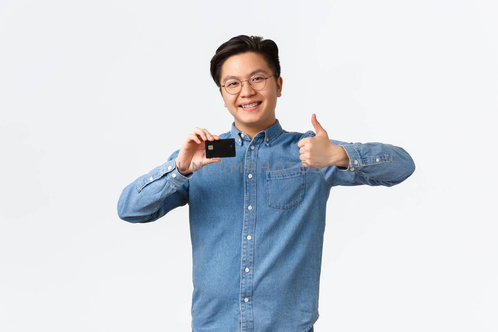 Satisfied young asian male entrepreneur, starting own startup, open bank account, showing thumbs-up in approval, recommend use credit card, standing white background pleased.
