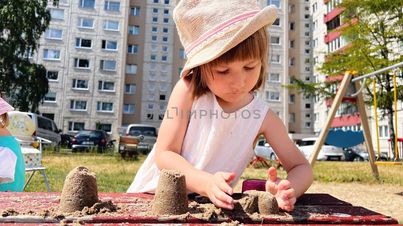 SMALL GIRL IN SUMMER DRESS playing with sand in the backyard of urban block houses in Tallinn, Estonia