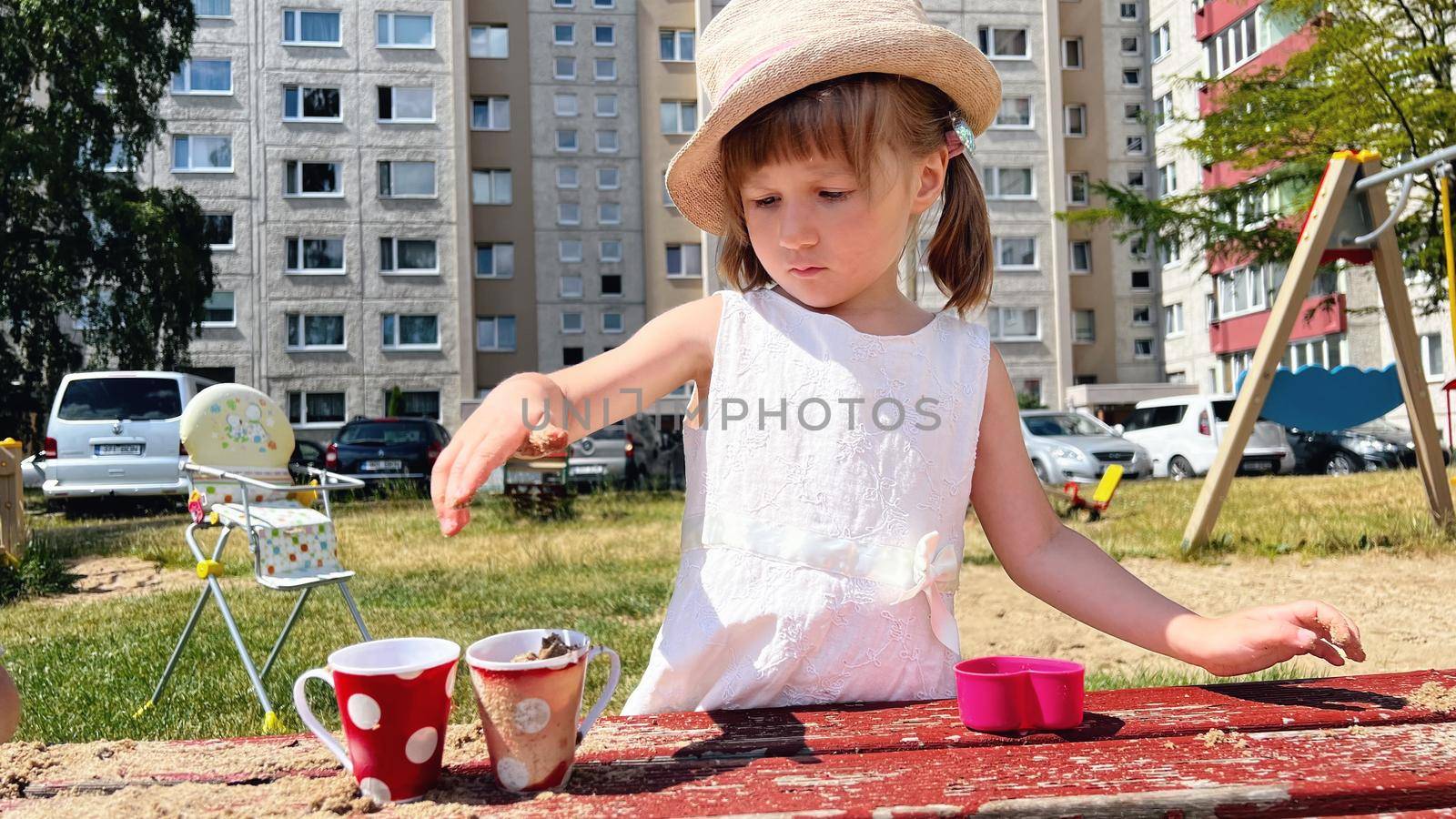 SMALL GIRL IN SUMMER DRESS playing with sand in the backyard of urban block houses in Tallinn, Estonia