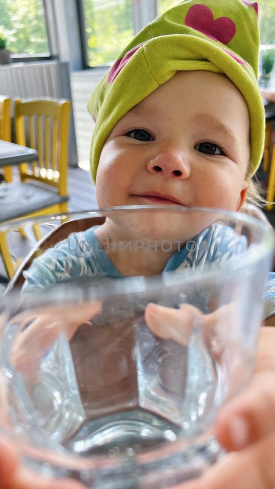 Small girl sitting at the table and showing glass of water into camera and making a funny face