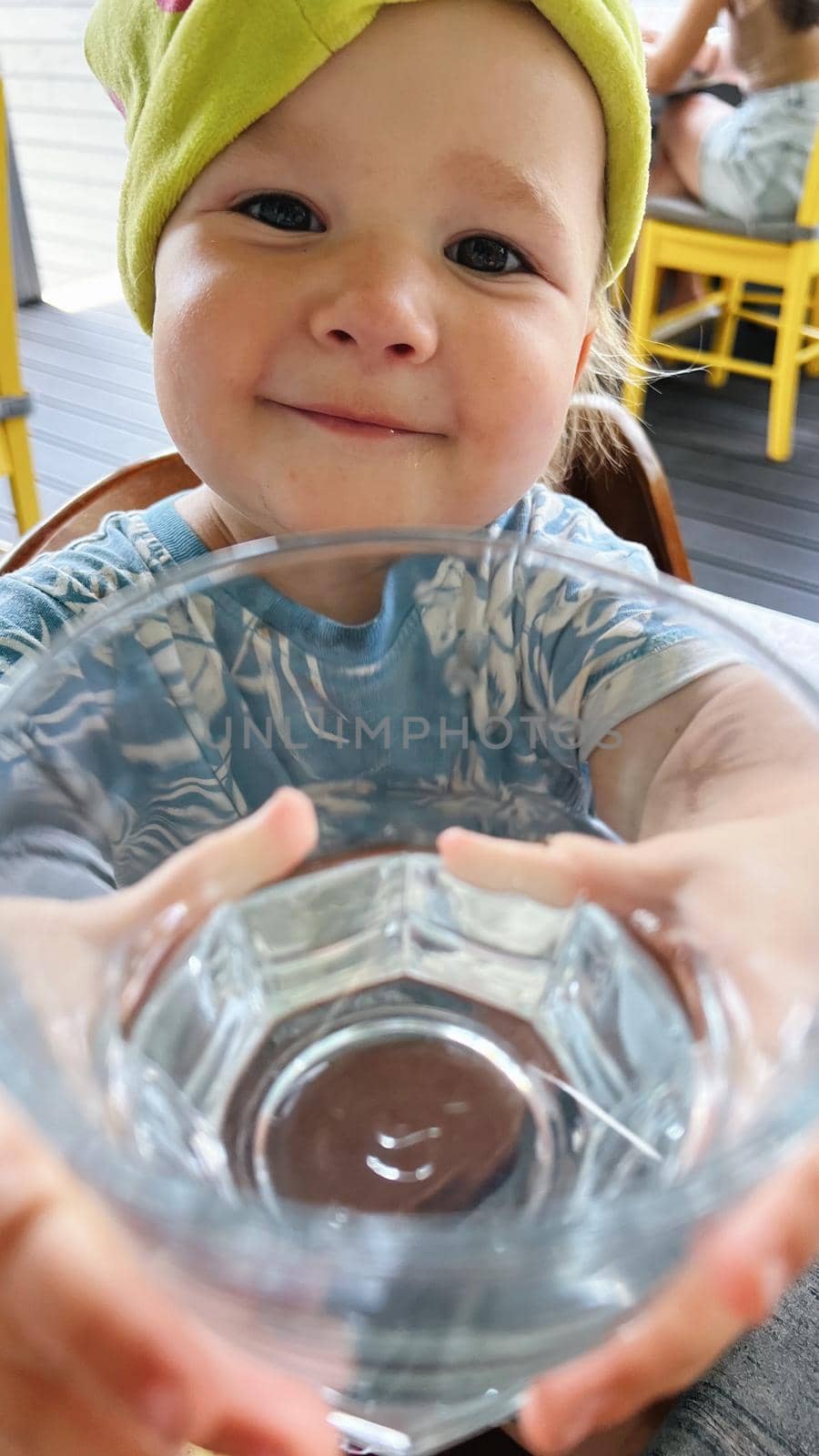 Small girl sitting at the table and showing glass of water into camera and making a funny face