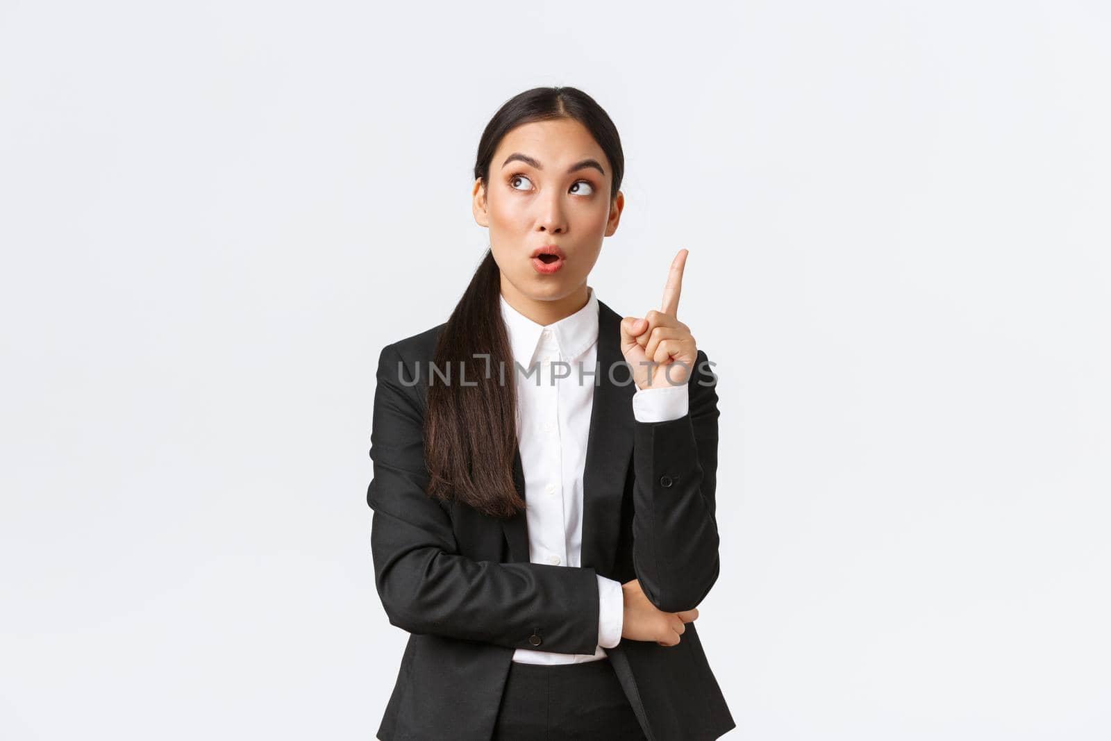 Smart and creative asian businesswoman have excellent idea, raising finger up and looking upper left corner thoughtful, suggest solution, make plan, saying thought over white background.
