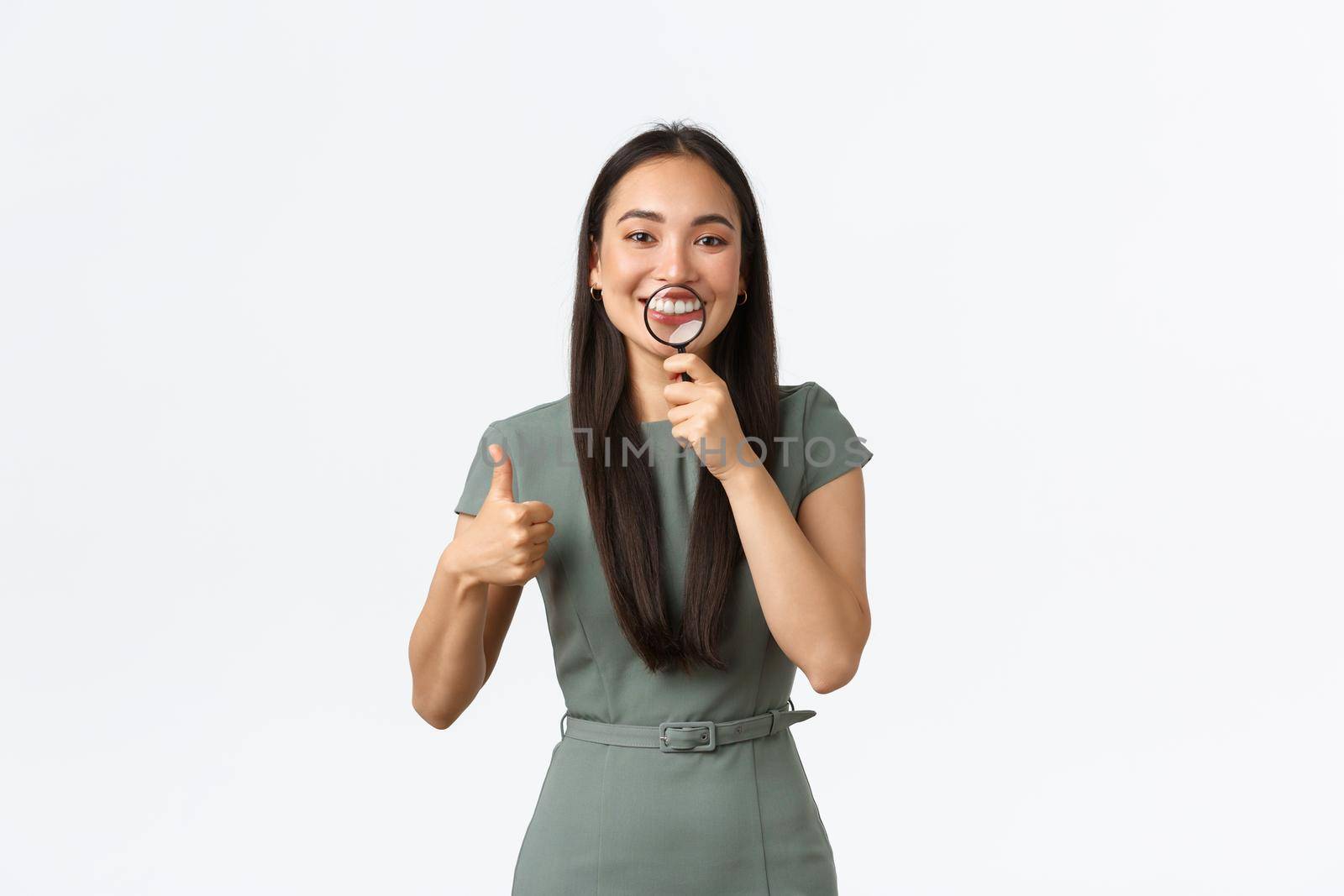 Healthcare, beauty and stomatology concept. Satisfied attractive asian woman whiten teeth at dentist office, showing perfect smile with magnifying glass over mouth and make thumbs-up in approval by Benzoix