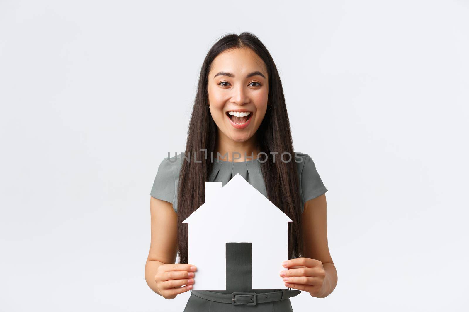 Insurance, loan, real estate and family concept. Cheerful asian female buying or selling home, holding paper house and smiling upbeat, searching for new apartment, white background.