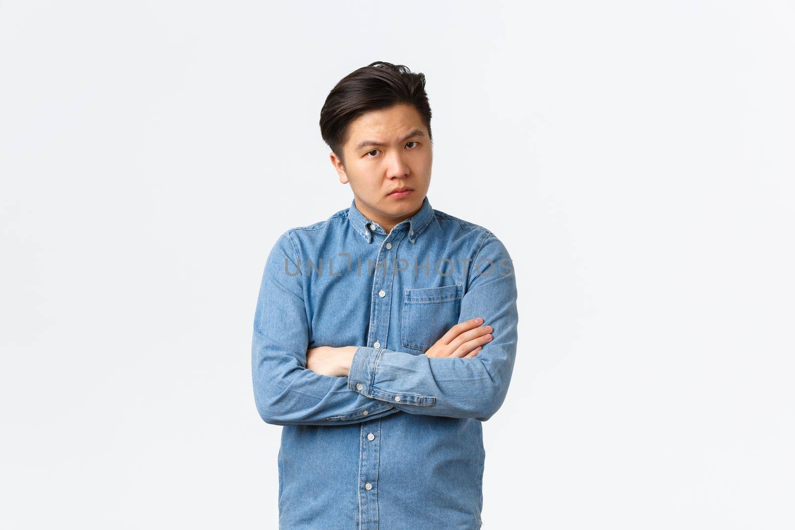 Skeptical and judgemental serious asian man standing with arms crossed and looking disappointed at camera, scolding someone bad behaviour, frowning upset, standing white background.