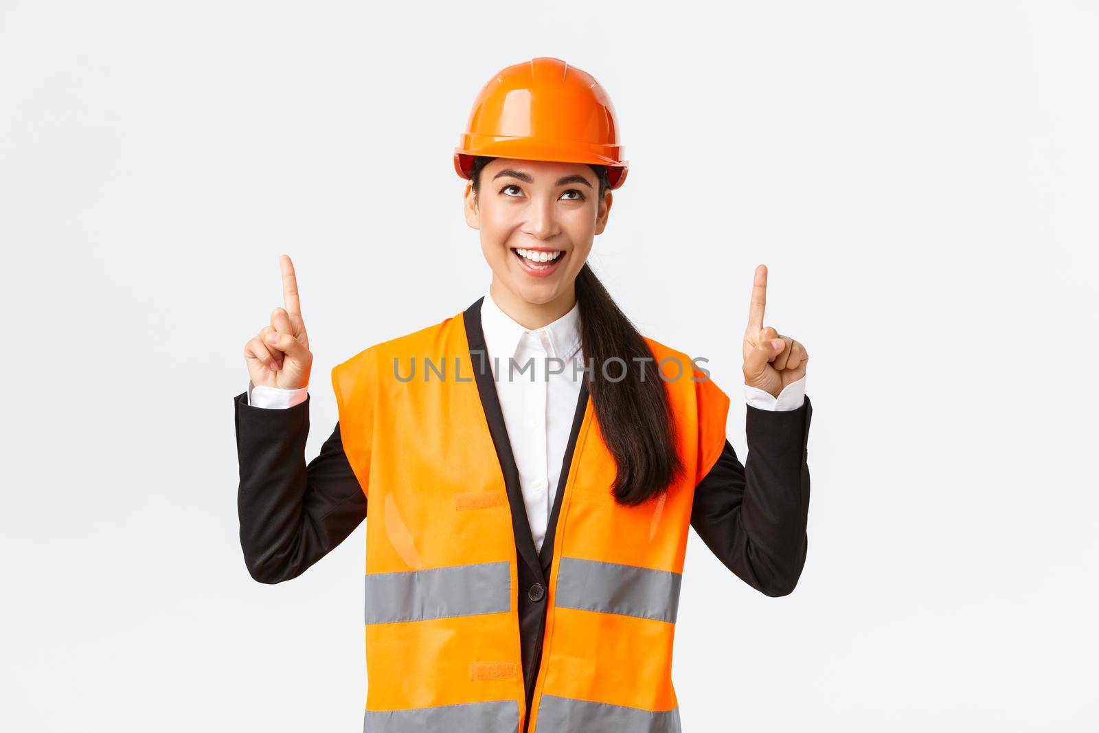 Building, construction and industrial concept. Successful pleased asian female engineer in safety helmet inspect object, looking and pointing fingers up satisfied. Architect pleased with good result.