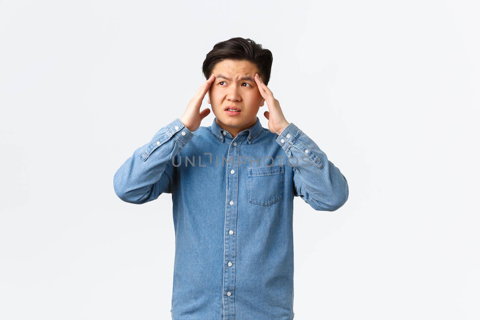 Troubled and uneasy asian man looking perplexed, having complicated situation. Guy with headache touching head and looking away, suffering painful migraine, standing white background by Benzoix