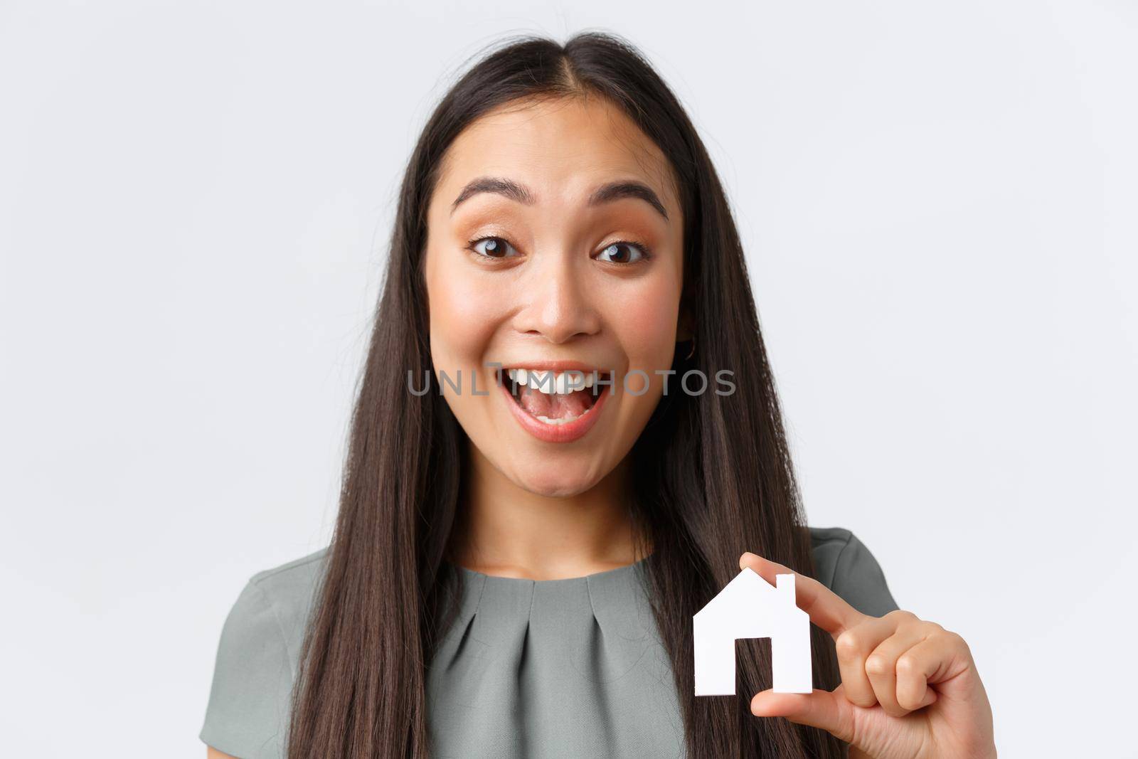Insurance, loan, real estate and family concept. Excited smiling asian woman found perfect place to buy or rent, showing small house in hands and rejoicing, buying home, standing white background by Benzoix