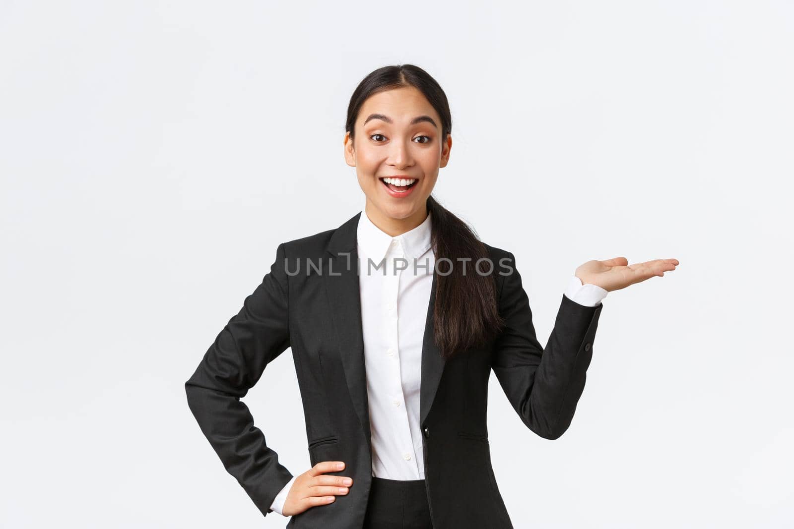 Excited smiling saleswoman introduce product, trying sell something over white copyspace. Pretty asian female manager showing project, pointing hand right and looking upbeat, white background.