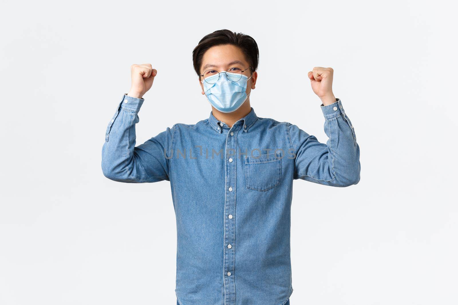 Covid-19, preventing virus, and social distancing at workplace concept. Successful winning asian businessman encourage good team spirit, raising hands up in rejoice, wearing medical mask.