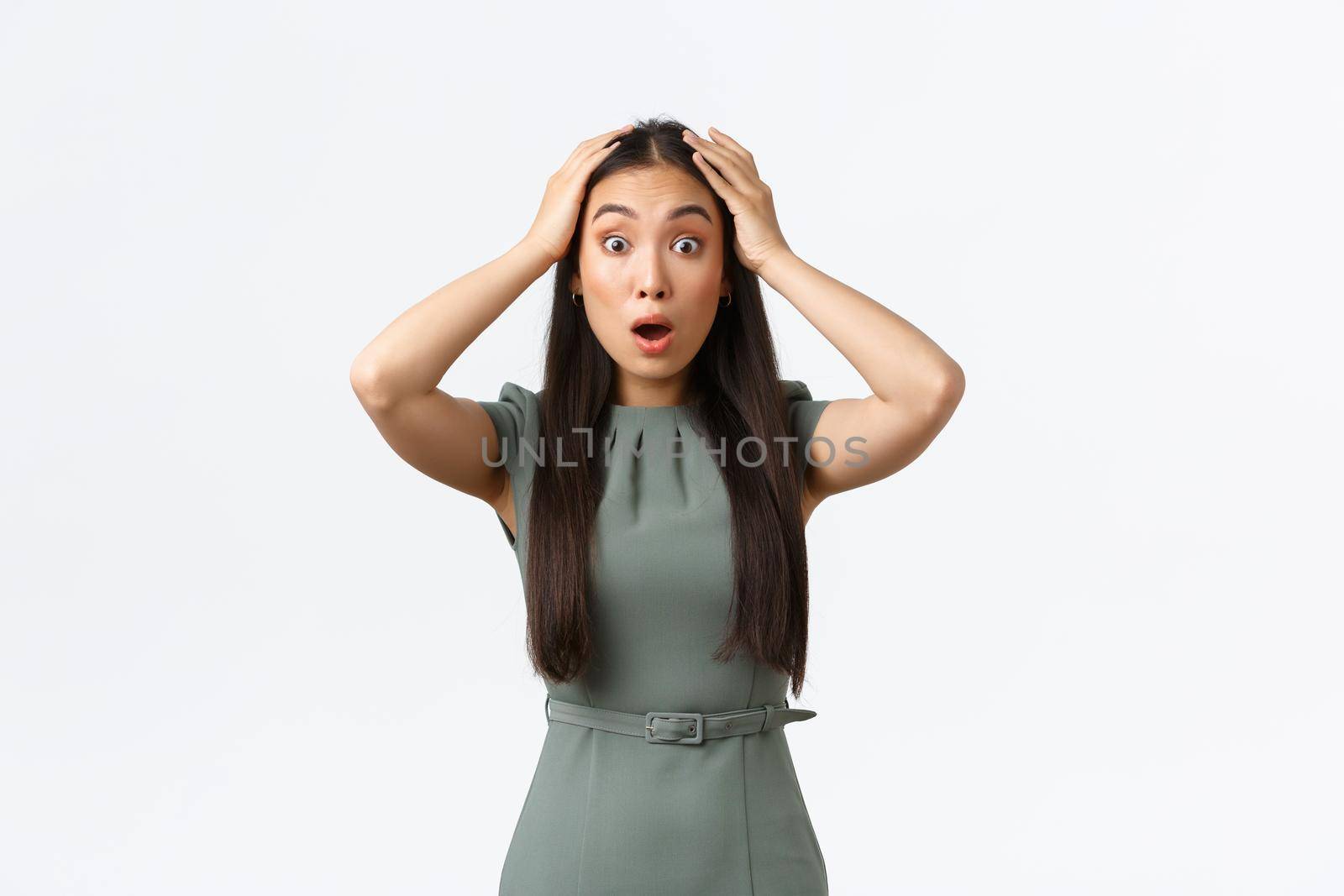 Small business owners, women entrepreneurs concept. Surprised and astounded asian businesswoman in dress, grab head shocked and stare speechless at camera, drop jaw amazed, white background.