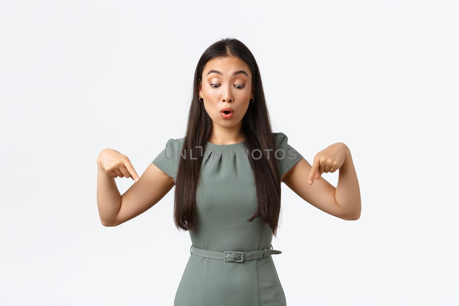 Small business owners, women entrepreneurs concept. Shocked and amazed asian woman in dress, businesswoman pointing fingers down, female stare down at announcement, white background.