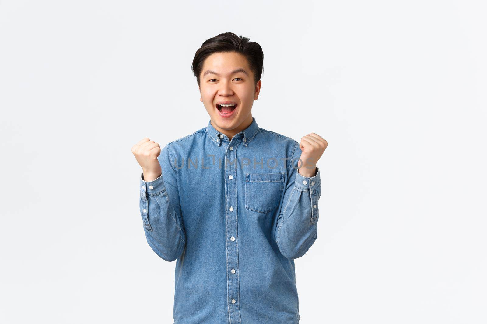 Smiling happy asian man fist pump and saying yes with satisfied smile as winning, celebrating victory, achieve goal, receive scholarship or promotion, rejoicing over white background.