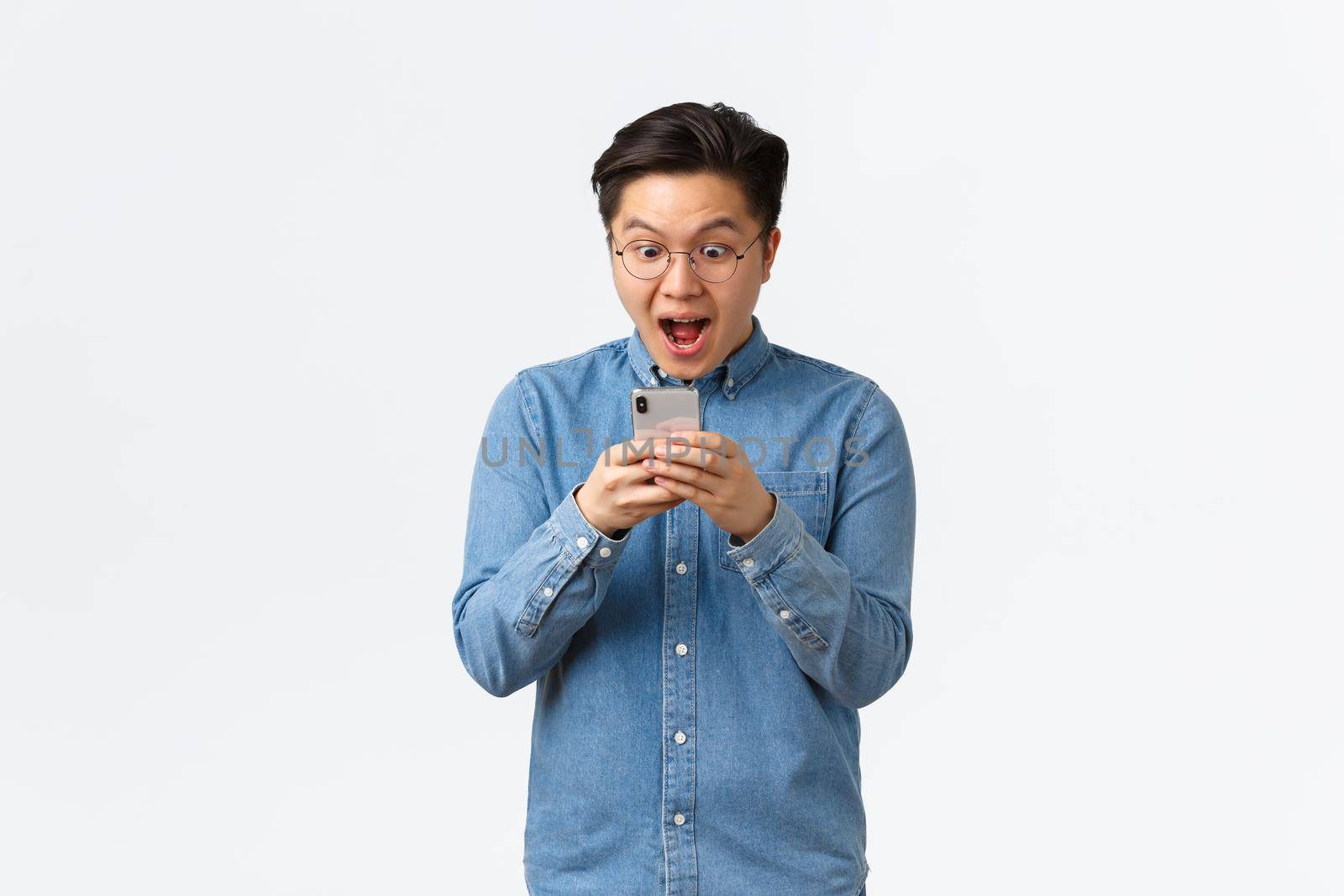 Excited guy seeing new awesome application or social network post of favorite blogger, looking amazed and happy at mobile phone screen, standing amused over white background.