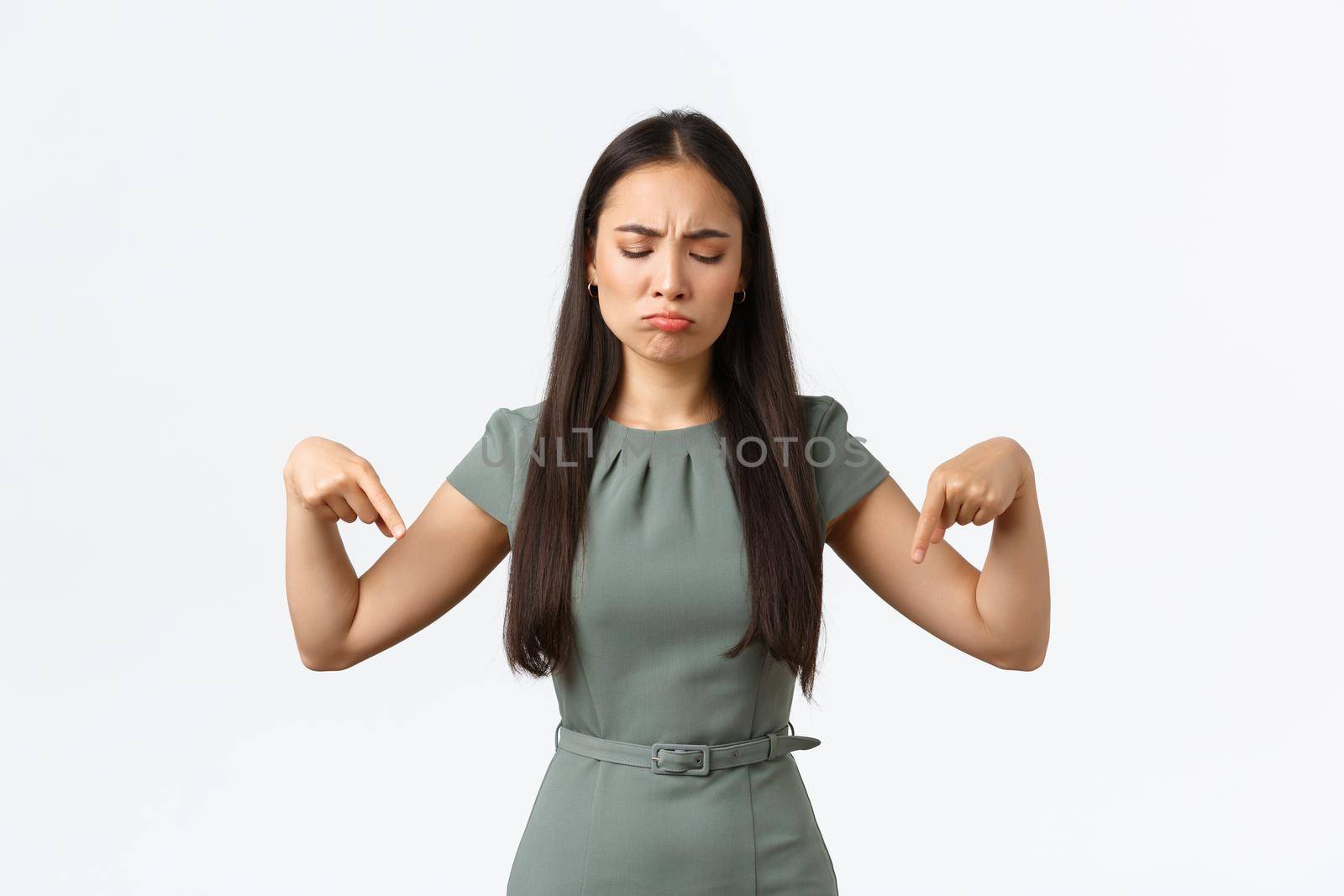 Small business owners, women entrepreneurs concept. Disappointed gloomy asian woman complaining unfair situation, looking with regret and jealousy, pointing fingers down upset.