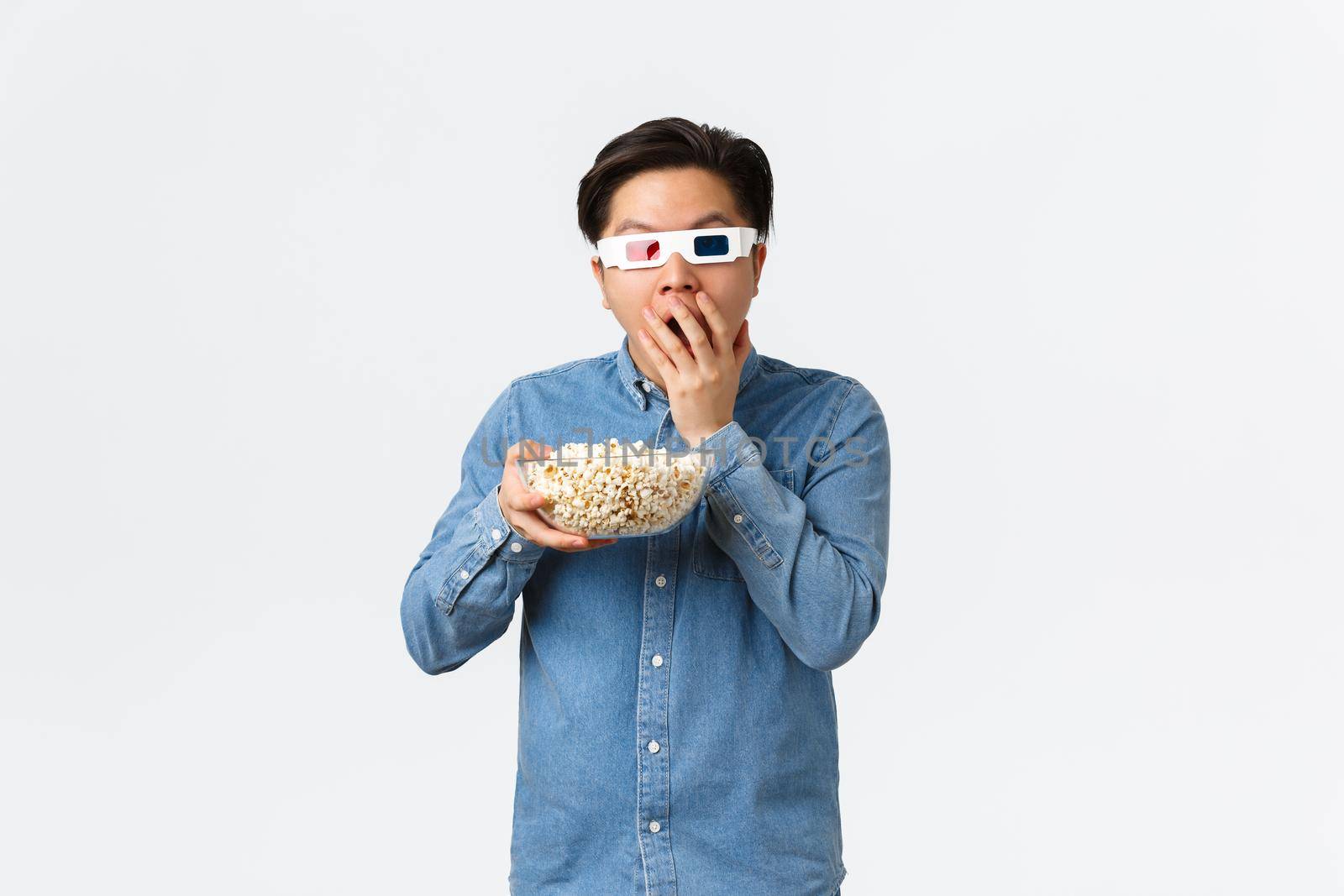 Leisure, lifestyle and people concept. Astonished asian guy in 3d glasses munching popcorn excited looking at TV, watching movie on wide screen, attend cinema, standing white background by Benzoix