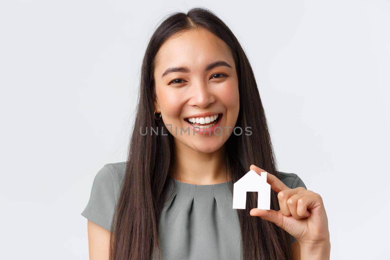 Insurance, loan, real estate and family concept. Close-up of smiling beautiful asian woman buying apartment, found perfect home, showing small paper house and laughing, white background by Benzoix