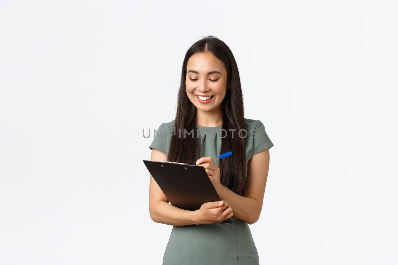 Pretty young asian female entrepreneur, small business owner fill in blank form for shipping, writing on clipboard, smiling enthusiastic as prepare list of order receivers, delivering to clients.