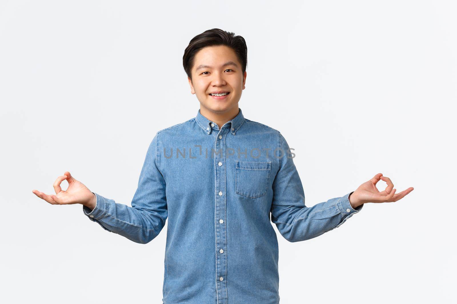 Cute asian man with braces meditating, smiling peaceful and relaxed, reaching nirvana or zen, standing in lotus pose with hands spread sideways, doing yoga exercises to chill, white background by Benzoix